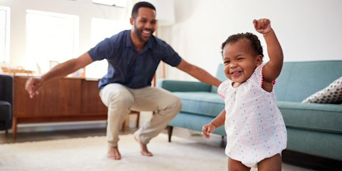 Father squatting and and playing with a laughing toddler 