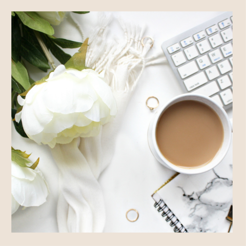 A white flower placed next to a cup of coffee and keyboard